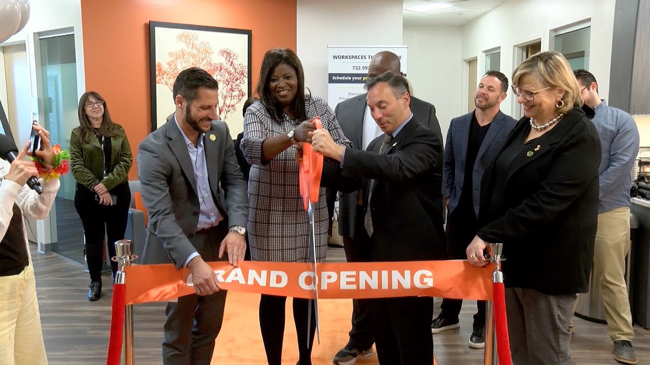 A group of people at a ribbon-cutting ceremony for a grand opening inside an office space.