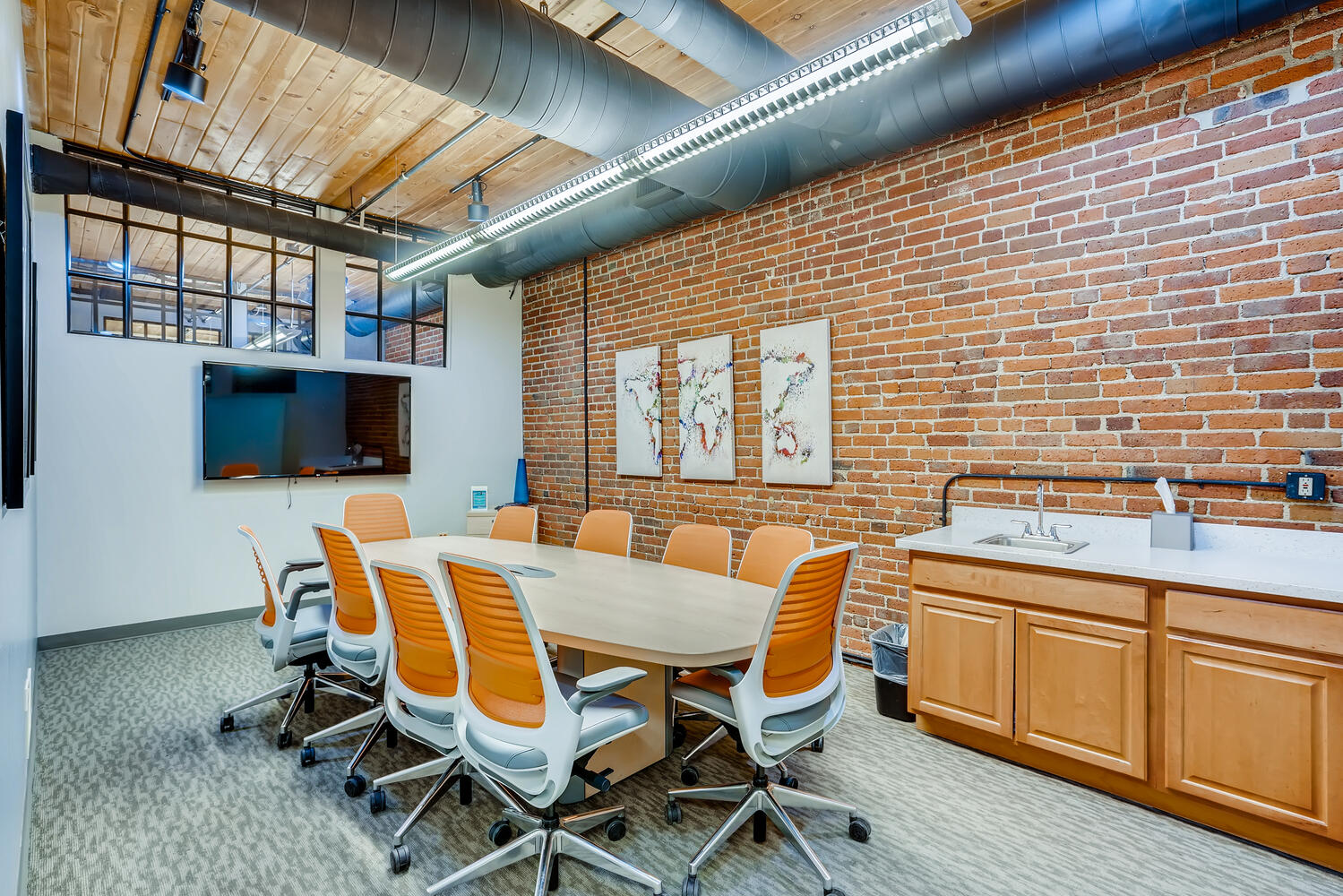 Modern office conference room with brick wall, large screen, and conference table for office evolution franchising meeting space.
