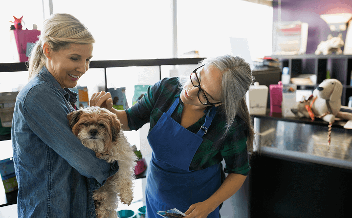 Two women, one with a dog, engaging in a friendly conversation at a franchise office, showcasing community and customer service.
