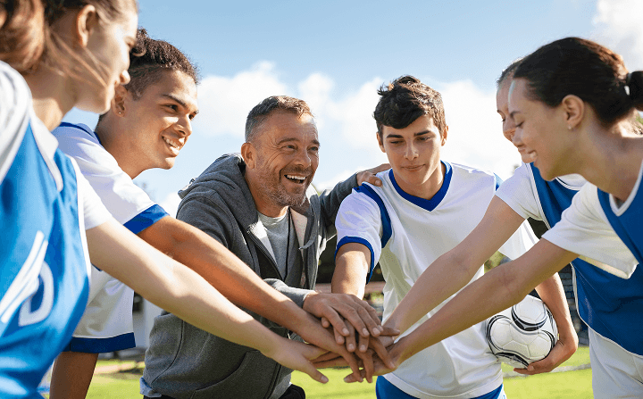 A diverse group of young soccer players and their coach in a team huddle, showing unity and teamwork during a match.